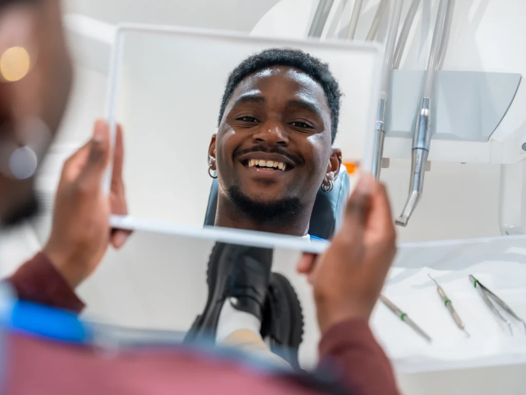 Man smiling in mirror after teeth cleaning in Wiggins, MS